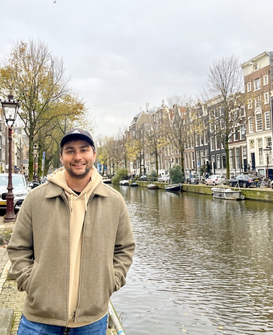 Andrew standing in a brown jacket in front of Amsterdam canal